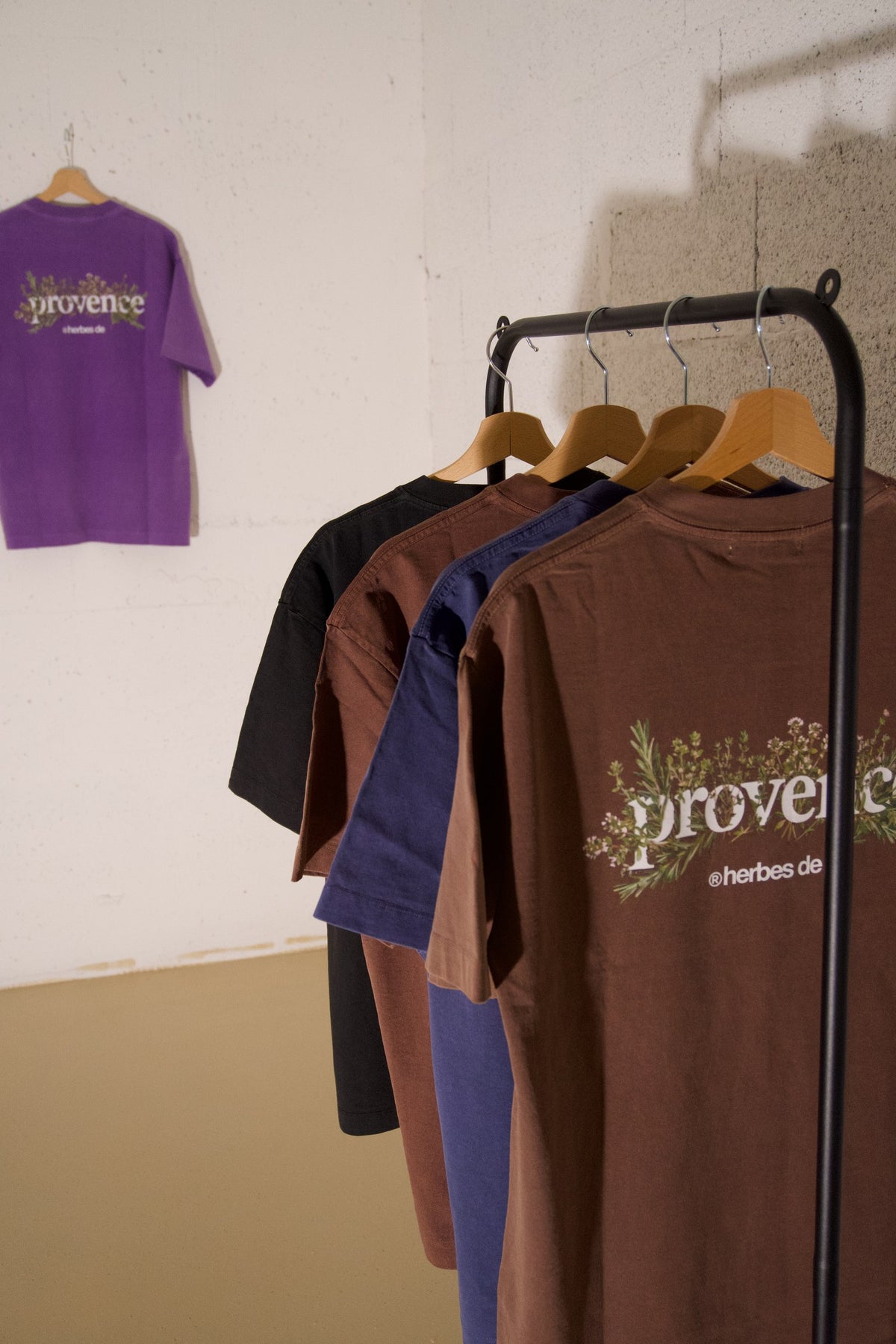 T-shirts COA sur un portant, avec Herbes de Provence Argile au premier plan